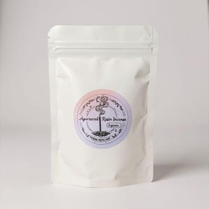 May include: A white, resealable pouch with a circular label featuring the text "Agarwood Resin Incense" and a stylized illustration of incense smoke. The label has a pink and purple gradient. The pouch contains 8 grams of incense.