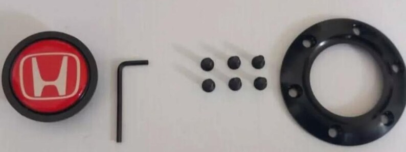 Pu&ograve; includere: Un set di componenti per auto, tra cui un emblema Honda rosso e bianco, un anello circolare nero con fori per bulloni, sei bulloni neri e una chiave a brugola nera. L'emblema &egrave; rotondo e presenta il logo Honda bianco.