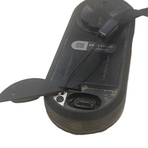 May include: A black device with a charging port and a black strap attached. The device has a small black cover that can be removed to reveal the charging port. The device has a label that reads "VARTL515 2044503".