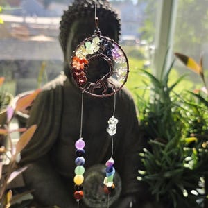 May include: A hanging ornament featuring a circular copper wire frame shaped like a tree, adorned with multi-colored gemstone chips. Two vertical strands hang from the frame, each decorated with colorful beads and a clear faceted crystal prism.