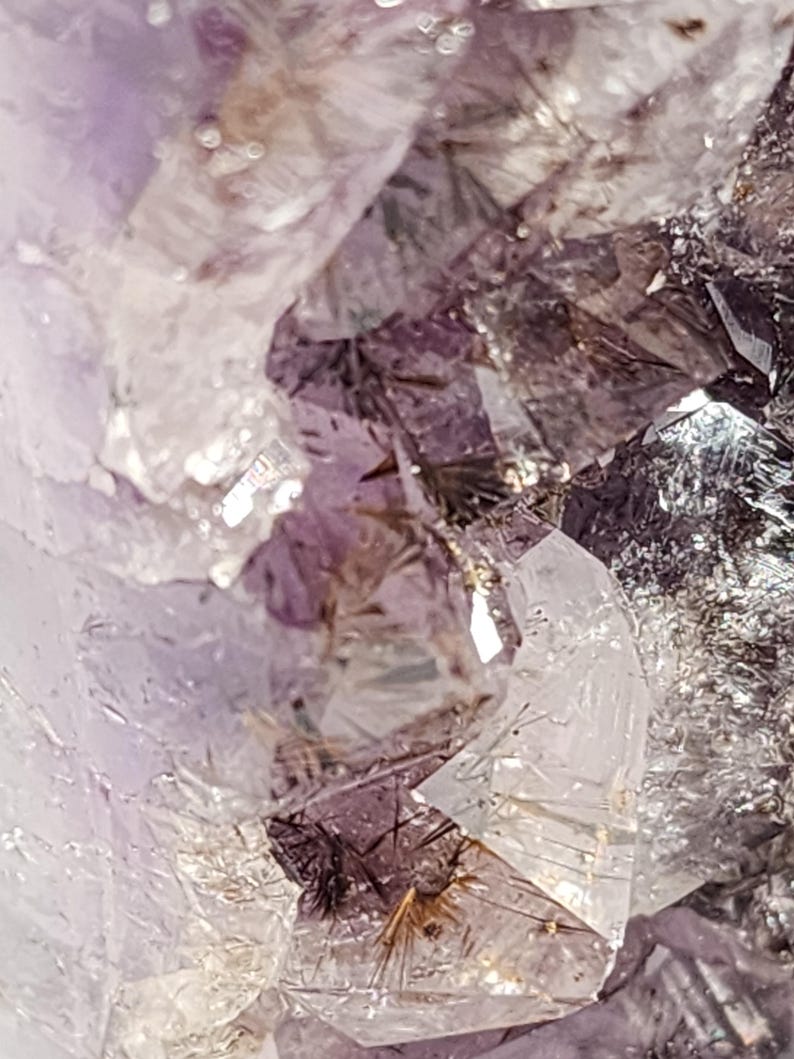 May include: Close-up of a cluster of amethyst crystals. The crystals display a range of colors, from deep purple to translucent white. The facets of the crystals catch the light, creating a sparkling effect. The overall texture is rough and natural.