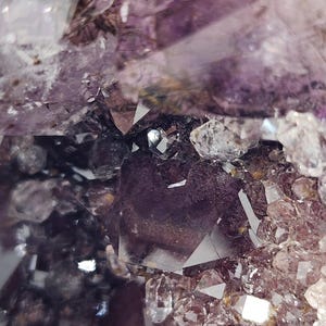 May include: Close-up of a cluster of amethyst crystals. The crystals display a range of purple hues, from deep violet to pale lavender, with clear, crystalline points. The image highlights the natural, geometric formations of the mineral.