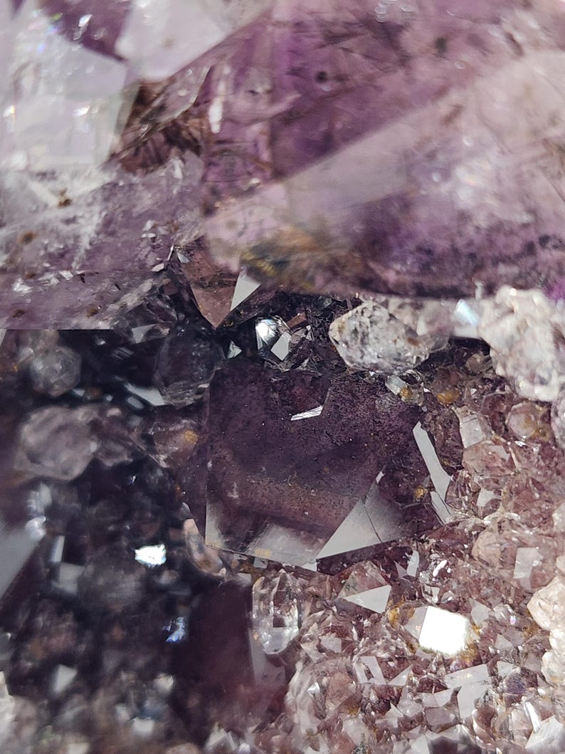 May include: Close-up of a cluster of amethyst crystals. The crystals display a range of purple hues, from deep violet to pale lavender, with clear, crystalline points. The image highlights the natural, geometric formations of the mineral.