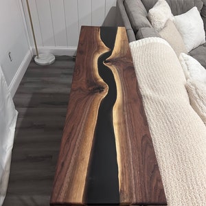May include: A long, narrow console table with a black epoxy river running through the center of the walnut wood top. The table has hairpin legs.