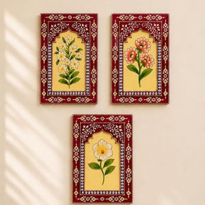 May include: Three rectangular wall plaques featuring deep red frames with intricate white floral patterns surrounding a central yellow panel. Each panel displays a hand-painted botanical illustration of flowers in white, orange, and yellow hues.