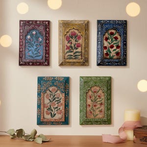 May include: Five framed floral art pieces with ornate, colorful borders. Each frame features a different color: burgundy, gold, blue, teal, and green. The artwork inside each frame depicts a floral design with red, pink, and white flowers.