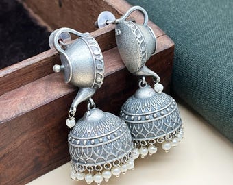 May include: Silver tone earrings with a teapot design and a dangling bell-shaped charm with pearl accents.