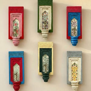 May include: A collection of six colorful, rectangular wall decor pieces. Each piece features a painted floral design within a framed archway, with varying colors including red, pink, green, blue, yellow, and gray. The bases are decorative.