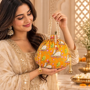 May include: A vibrant yellow drawstring pouch bag featuring a repeating pattern of white cows, pink lotus flowers, and green leaves. The bag has a beaded pearl handle and gold-toned drawstring cords with decorative metal tassels at the ends.