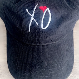 May include: Black corduroy baseball cap with white embroidered "XO" and a red heart.