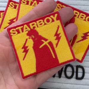 May include: Embroidered square patches in yellow and red, featuring a red figure with lightning bolts and the word "STARBOY". Several patches are visible. These patches are likely for clothing or accessories.