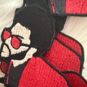 May include: A set of four embroidered iron-on patches featuring a cartoon character with black hair, red sunglasses, and a red jacket. The patches are black, red, and white.