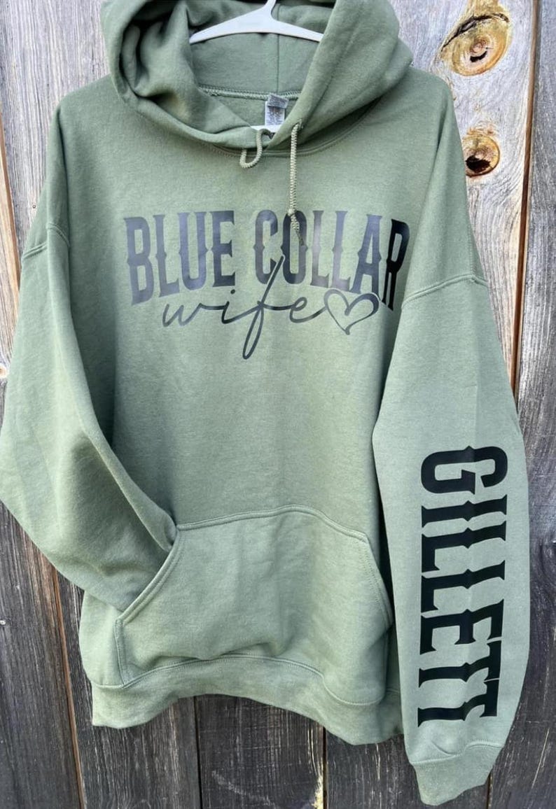May include: A green hooded sweatshirt with the text "BLUE COLLAR wife" and a heart on the front. The left sleeve has the word "GILLETTE" printed vertically down the sleeve.