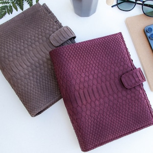 Peut inclure: Deux journaux reliés en cuir avec un motif de peau de serpent. L'un est brun et l'autre est bordeaux.