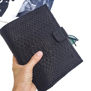 May include: A black snakeskin clutch bag with a flap closure and a snap button.