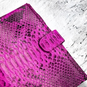 Peut inclure: Un portefeuille en cuir magenta vif avec une texture de peau de reptile. Le portefeuille est doté d'une fermeture à rabat avec une languette texturée assortie. Le fond est un motif abstrait contrasté blanc et noir.