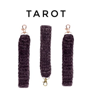 May include: Three dark purple fuzzy keychains with gold clasps. The keychains are arranged in a row with the word "TAROT" printed above them.