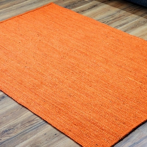 May include: A close-up of a bright orange woven rug made of natural fibres. The rug has a textured surface and a slightly rough feel.