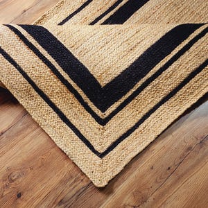 Op de afbeelding: Een vloerkleed van natuurlijke vezels met zwarte strepen. Het vloerkleed is gemaakt van jute en heeft een natuurlijke, aardse uitstraling.