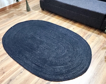 May include: A navy blue oval jute rug. The rug is made of woven fibers and has a textured surface. The rug is placed on a hardwood floor.