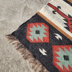 May include: A black, red, and green patterned rug with fringe. The rug has a geometric design with a white and brown background.