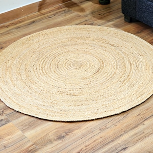 Può includere: Un tappeto rotondo in fibra naturale con una trama tessuta. Il tappeto è di colore marrone chiaro e presenta un motivo circolare.