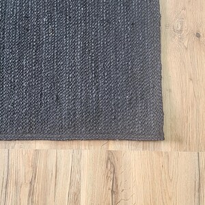May include: A dark gray woven rug with a textured surface. The rug is placed on a light wood floor.