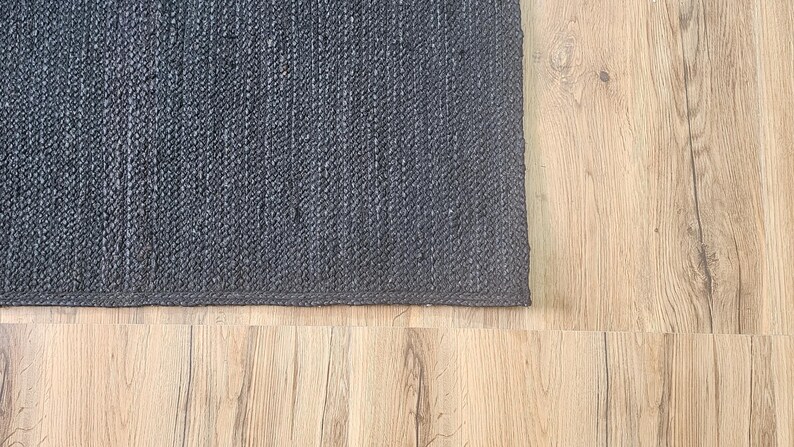 May include: A dark gray woven rug with a textured surface. The rug is placed on a light wood floor.