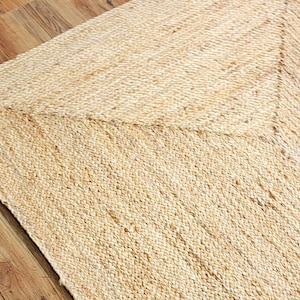 May include: A rectangular area rug crafted from natural tan jute fibers, featuring a woven texture with a distinct chevron pattern created by the directional alignment of the braided material across the surface of the floor covering.