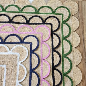 Puede incluir: Cinco alfombras de yute con bordes de diferentes colores. Los bordes son festoneados y presentan un ribete blanco, negro, rosa y verde. Las alfombras están apiladas, con la alfombra más grande en la parte inferior y la más pequeña en la parte superior.