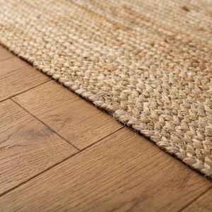 May include: A rectangular area rug crafted from natural tan jute fibers woven in a tight, braided herringbone pattern. The rug features a thick, textured surface with visible variations in the light brown and beige tones of the plant-based material.