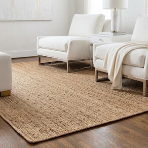 May include: A rectangular area rug crafted from natural tan jute fibers with a woven texture. The rug features a consistent, earthy brown tone and a flat-weave construction, providing a neutral foundation that covers the dark wooden floor.