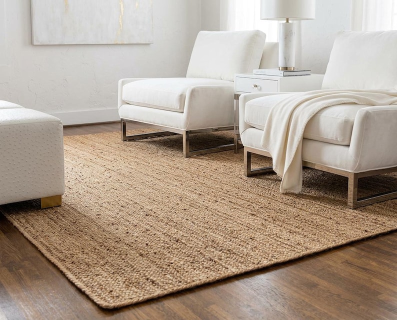 May include: A rectangular area rug crafted from natural tan jute fibers with a woven texture. The rug features a consistent, earthy brown tone and a flat-weave construction, providing a neutral foundation that covers the dark wooden floor.