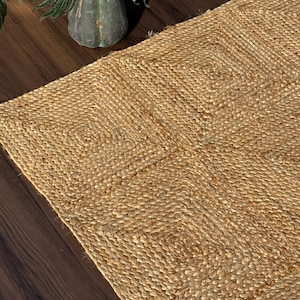 Op de afbeelding: Een rechthoekig vloerkleed gemaakt van natuurlijke bruine jutvezels, met een herhalend geometrisch ruitpatroon dat in de textuur is geweven. Het kleed vertoont een grove, gevlochten constructie met zichtbare variaties in het plantaardige materiaal.