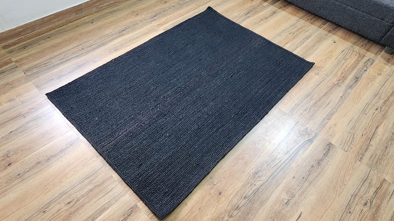 May include: A black woven rug with a textured surface. The rug is laid out on a wooden floor.