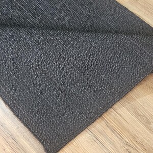 May include: A black woven rug with a textured surface. The rug is folded in half and lying on a wooden floor.