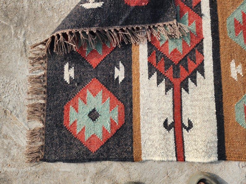 May include: A black, white, red, and green patterned rug with a fringe border. The rug has a geometric design.