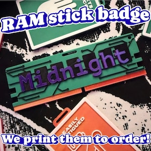 May include: A rectangular RAM stick badge featuring a teal green circuit board design with a black center strip and the word Midnight embossed in purple lettering. The bottom edge is orange, and the badge includes a small hole for attachment.