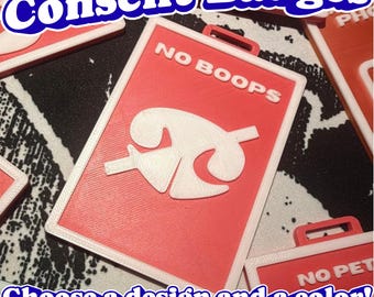May include: A rectangular red badge with a white border and a white loop at the top. The badge features the white text NO BOOPS and a white graphic symbol of a nose with a diagonal line through it, indicating a request for no physical contact.