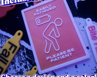 May include: A rectangular peach-colored badge with a white border featuring a white line-art icon of a person leaning over with a low battery symbol above them. The text reads EASILY FATIGUED and PLEASE BE PATIENT in white raised lettering.