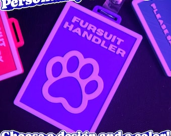 May include: A rectangular purple badge with a white border and a white paw print icon. The text FURSUIT HANDLER is printed in white capital letters. The badge features a top attachment point for a lanyard, showcasing a clean and functional design.