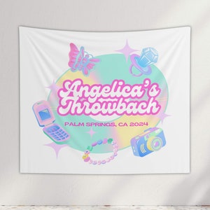 May include: A white tapestry with a pink and blue design. The design features a circle with the text "Angelica's Throwback" in pink letters. The circle is surrounded by a butterfly, a flip phone, a camera, and a beaded necklace. The text "PALM SPRINGS, CA 2024" is below the circle.