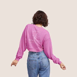 May include: A pink cropped sweatshirt with long sleeves and a white graphic on the back that says "Allison's Velvet Vows Bachelorette Weekend 20 21".