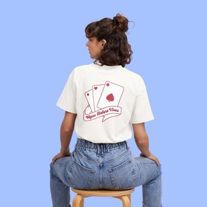 May include: White t-shirt with a red graphic of playing cards and the text "Vegas Before Vows".