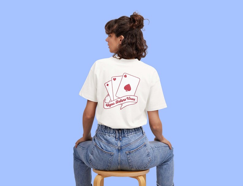 May include: White t-shirt with a red graphic of playing cards and the text "Vegas Before Vows".
