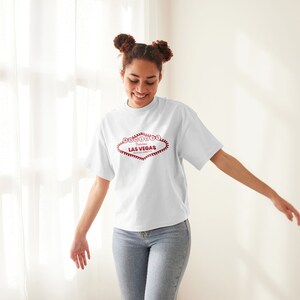May include: A white t-shirt with a red graphic of the "Welcome to Fabulous Las Vegas" sign.