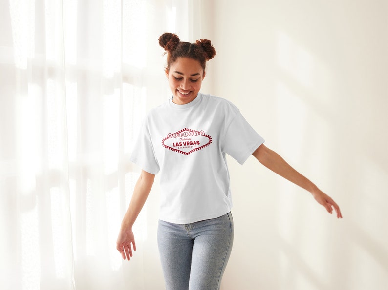May include: A white t-shirt with a red graphic of the "Welcome to Fabulous Las Vegas" sign.
