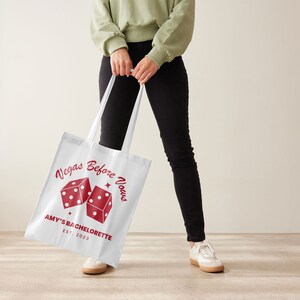 May include: White tote bag with red dice and the text "Vegas Before Vows" and "Amy's Bachelorette Est. 2023".