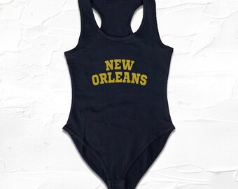 May include: A black sleeveless bodysuit with a gold "NEW ORLEANS" graphic on the front.