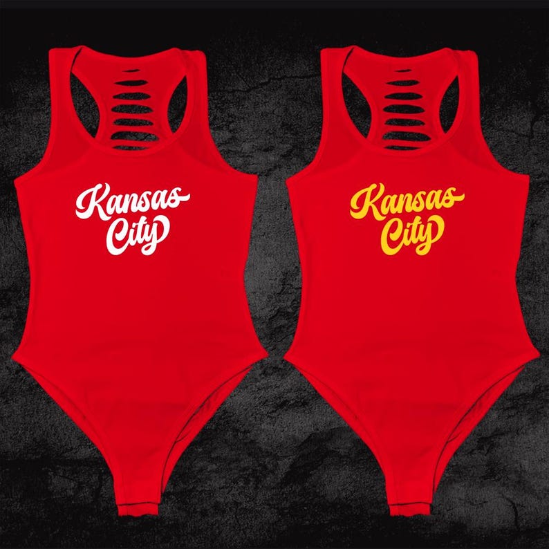 Może przedstawiać: Dwa czerwone tank topy z wyciętym tyłem. Jeden tank top ma napis "Kansas City" białymi literami. Drugi tank top ma napis "Kansas City" ż&oacute;łtymi literami.